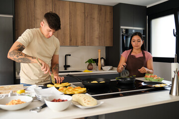 Two young latin people cooking traditional arepas and llapingachos at kitchen.