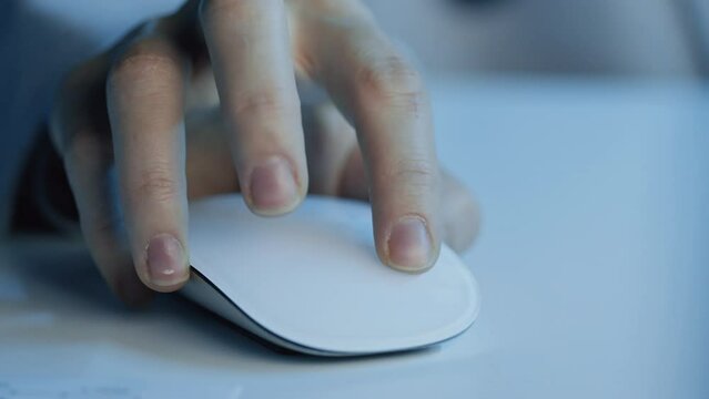 Panning left extreme close up of unrecognizable person sitting at desk using computer mouse indoor at night time