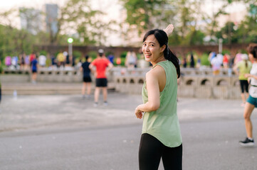 Fototapeta na wymiar Female jogger. Fit young Asian woman with green sportswear aerobics dance exercise in park and enjoying a healthy outdoor. Fitness runner girl in public park. Wellness being concept