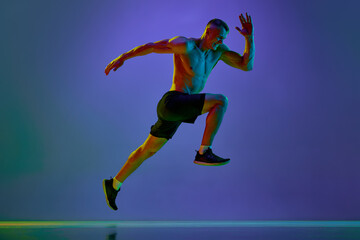 Fototapeta na wymiar Dynamic image of young man with muscular, strong, fit body, professional runner in motion against blue studio background in neon light