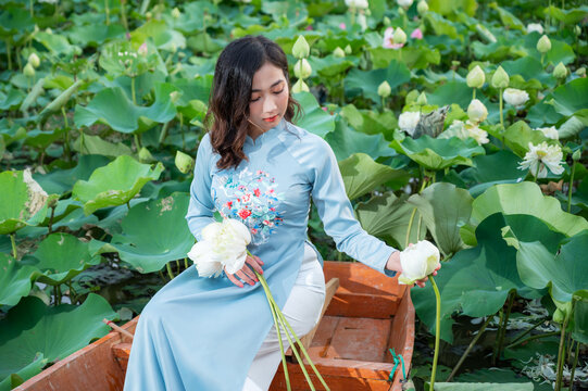 Vietnamese woman wearing Ao dai costume sitting on a boat in a lotus pond.