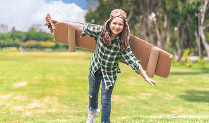 Caucasian girl playing in the garden wearing paper wings and holding a wooden airplane running around having fun dreaming of having a career as a pilot when she grows up to be an adult in future