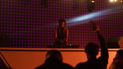 Portrait of attractive female techno DJ performing playing her music set on a stage in front of crowd in a nightclub during a festival, bright flashing stage lights, huge LED screen behind talent
