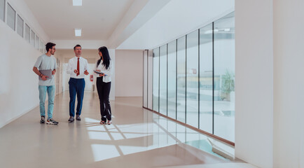 Business couple young entrepreneurs with laptops, walking alongside their boss, as they navigate the corridors of a modern corporate building, embodying collaboration, innovation, and ambition in the