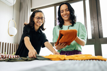 Mom and teen daughter bond as they fold laundry in bed, creating cherished memories through shared...