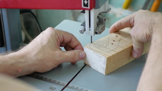 A violin maker cuts a blank for making a violin scroll on a bandsaw, close-up.