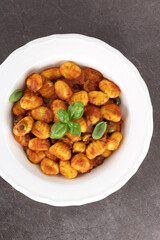 Traditional Italian potato gnocchi with tomato sauce and fresh basil on brown background. Top view.