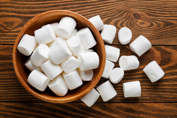 Marshmallows in a plate and scattered on a wooden background. Top view