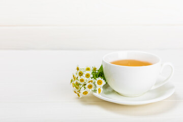 Chamomile herbal tea in a cup on a white wooden table with a bouquet of chamomile. Close-up. Copy space. Useful herbal drinks, immunity tea. Natural healer concept.Place for text.