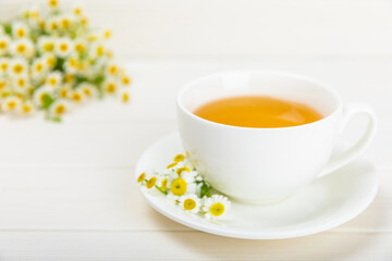 Chamomile herbal tea in a cup on a white wooden table with a bouquet of chamomile. Close-up. Copy space. Useful herbal drinks, immunity tea. Natural healer concept.Place for text.