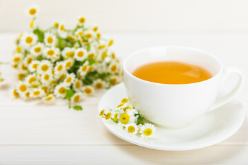 Chamomile herbal tea in a cup on a white wooden table with a bouquet of chamomile. Close-up. Copy space. Useful herbal drinks, immunity tea. Natural healer concept.Place for text.