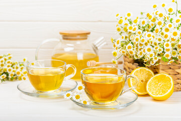 Chamomile herbal tea in a glass cup on a white wooden table with honey, lemon and chamomile...