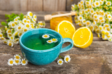 Chamomile herbal tea in a blue cup on a brown wooden table with honey, lemon and chamomile bouquet. Close-up. Copy space. healthy herbal drinks, immunity tea. Natural healer concept.Place for text.