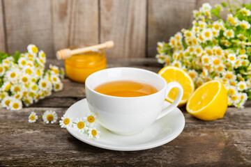 Fototapeta na wymiar Herbal chamomile tea in a cup on a brown wooden table with honey, lemon and chamomile bouquet. Close-up. Copy space. healthy herbal drinks, immunity tea. Natural healer concept.Place for text.