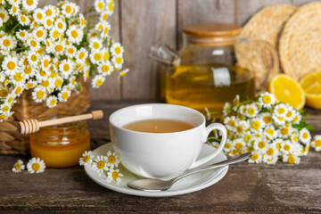 Herbal chamomile tea in a cup on a brown wooden table with honey, lemon and chamomile bouquet....