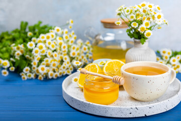 Chamomile herbal tea in a cup on a blue wooden table with honey, lemon and chamomile bouquet. Close-up. Copy space. healthy herbal drinks, immunity tea. Natural healer concept.Place for text.