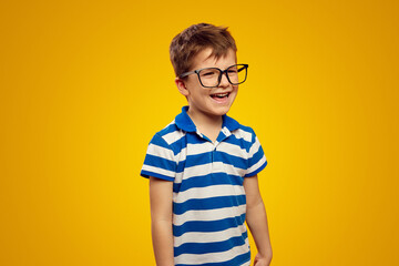 Happy positive schoolboy in blue striped polo shirt and glasses smiling and looking away while...