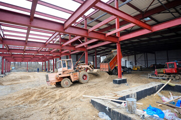 Fototapeta na wymiar Construction of the hangar. Backhoe working, truck uloading sand