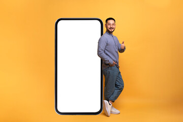 Mobile Offer. Excited asian guy leaning on big smartphone with blank screen