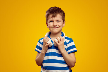 Naklejka premium Portrait of attractive little boy wearing blue striped polo shirt and wireless headset around his neck, isolated over yellow background