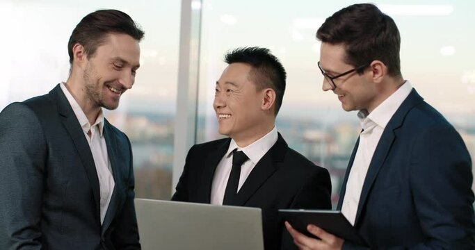 Sucessfull mixed-race managers having fun time during work. People with suits communicating and telling funny jokes in office. Loudly laughing while using technology devices. Business concept.