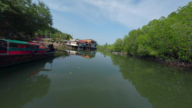 Flying close Asian village embankment boat water river local rural house green forest aerial view. FPV sport drone close low shot tropical countryside landscape port harbor fishing ship sunny scenery