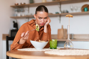 Taste trouble. Young caucasian woman showing dislike for her caesar salad, looking at it and dont...