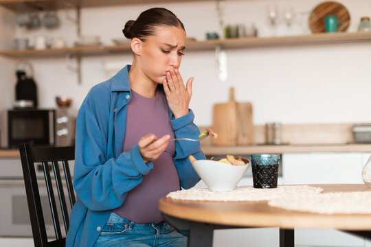 Toxicosis during pregnancy. Pregnant lady feeling nausea while looking at caesar salad during lunch at home