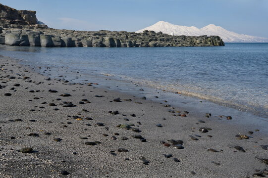 Russia. Far East, Kuril Islands. View of the Okhotsk coast of Iturup island with ash sand of volcanic origin against the background of two snow-covered volcanoes Chirip and Bogdan Khmelnitsky.