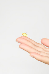 hand holding yellow vitamin capsule. taking vitamins and nutritional supplements for female beauty and health