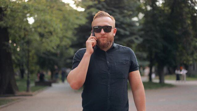 A happy bearded business man is walking around the city, talking on a mobile phone, solving a business case