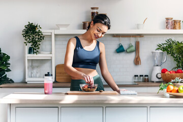Athletic woman eating a healthy bowl of muesli with fruit in the kitchen at home
