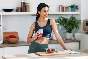 Athletic woman drinking healthy protein shake in the kitchen at home