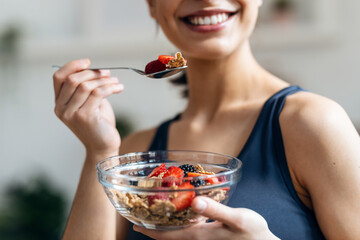 Athletic woman eating a healthy bowl of muesli with fruit in the kitchen at home