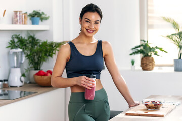 Athletic woman drinking healthy protein shake in the kitchen at home