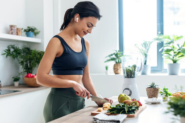 Shoot of athletic woman cutting fruits and vegetables to prepare a smoothie while listening to music with earphones in the kitchen at home