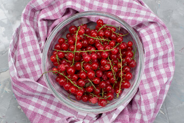 a top view red lingonberry inside round glass plate on the grey desk and purple tissue fruit berry color cranberry
