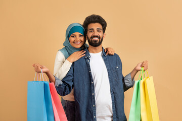 Happy Customers. Muslim Couple With Shopping Bags Posing Over Beige Studio Background