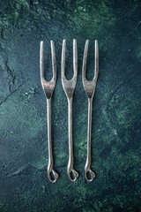 Above view of stainless steel buffet meat forks two tines on blue green background