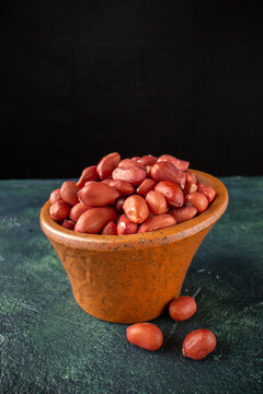 Close up view of red peanuts inside and outside of a brown pot on blue and black background