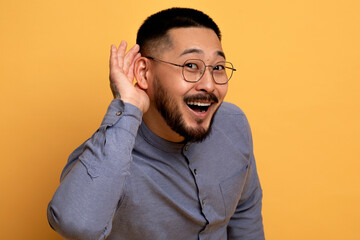 Curious Cheerful Asian Man Holding Hand Near Ear, Trying To Overhear Something