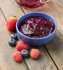Berries jam in a bowl with fruits over wooden table