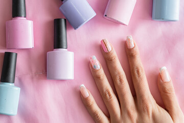 detailed view of a woman's hand with painted nails and colored nail polish next to it on a pink background