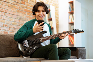 Obraz premium Cheerful Asian Teen Posing With Electric Guitar, Holding Smartphone Indoors