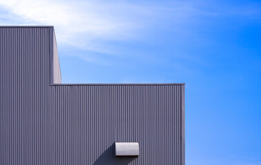 Grey corrugated metal wall with dryer vent of modern factory building against blue sky background