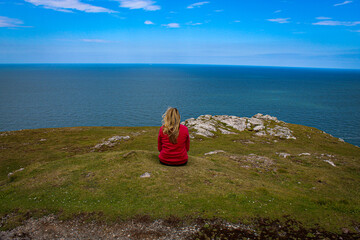 A lone woman on top of a mountain, she is sitting and staring out to sea, contemplating and thinking.