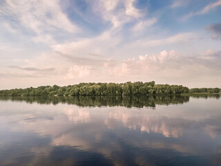 Beautiful summer landscape near the  water, blue cloudy sky and its reflection on the surface of water, view island in the middle of the river - 615188866
