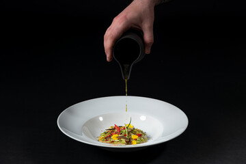 hand pouring sauce into a Gourmet and gastronomic dish isolated on a black background