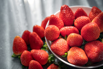 Bowl with strawberries on a stone table and sunscreens in close-up.