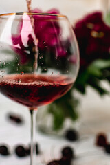 a glass of red wine next to flowers in a vase on a light background. cherries on the table. non-alcoholic wine.